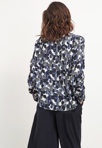 Blusa a maniche lunghe con un motivo astratto a pois blu navy e bianchi, realizzata in un tessuto leggero con una vestibilità leggermente ampia e polsini con bottoni.