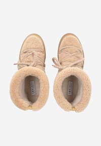 Bottines en shearling beige avec tissu texturé, bout arrondi et design à lacets. Doublure douce et semelle en caoutchouc visibles depuis la vue de dessus.