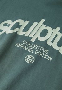 Žalias medvilninis marškinėliai su ryškiu baltu tekstu, rašančiu "sculpt" ir "COLLECTIVE APPAREL EDITION", su pasaulio ikona žemiau.