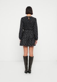 Μαύρο φόρεμα με σχέδια, μακριά μανίκια, βολάν στο τελείωμα και λεπτομέρεια με άνοιγμα στην πλάτη. Φορεμένο με καφέ μποτάκια μέχρι το γόνατο.