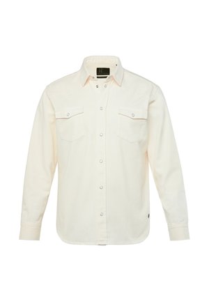 Camisa de manga larga en tela color crema con cierre de botones al frente, dos bolsillos en el pecho, botones a presión y dobladillo ligeramente curvado.