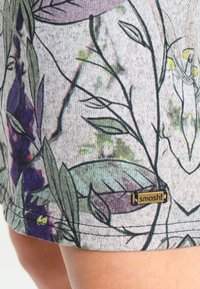 Shorts à motifs en tissu léger présentant des dessins floraux en violet et vert avec une finition texturée. Comprend une petite étiquette dorée « smash ! ».