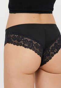 Culotte en coton noir et dentelle, avec un bord en dentelle florale le long des ouvertures des jambes et une ceinture lisse.