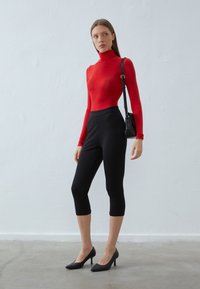 Rød langermet genser med høy hals, tettsittende; høyreiste svarte croppede leggings; svarte spisse hæler; tilbehør: liten svart crossover-sekk.