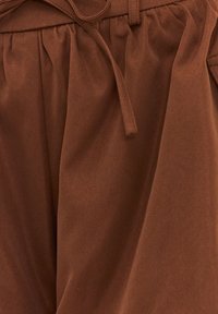 Pantalon marron taille haute avec taille froncée et ceinture en tissu nouée en nœud devant, en matière douce et légèrement texturée.