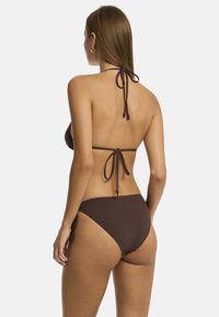 Model wearing a brown bikini, viewed from the back, with long hair and tied halter neck, showcasing minimalistic swimwear design.