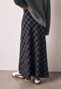 Jupe maxi à carreaux noirs avec des lignes grises et blanches, portée avec des baskets blanches. Pull gris en maille avec un détail rayé à l'ourlet.