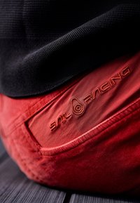 Röda bomullsbukser med ett texturerat svart tyg ovanför, med en broderad "Sail Racing"-logotyp i en kontrasterande nyans på bakfickan.