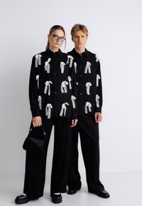 Μαύρα πουκάμισα με λευκά σχέδια κορδελών, σε συνδυασμό με φαρδιά μαύρα παντελόνια. Αξεσουάρ περιλαμβάνουν μια μικρή μαύρη τσάντα και χοντρά παπούτσια.