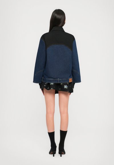 Traper jakna s crnim detaljima, opuštenog kroja, širokim rukavima i kontrastnim šavovima. Nosi se preko crne cvjetne suknje i crnih čarapa.