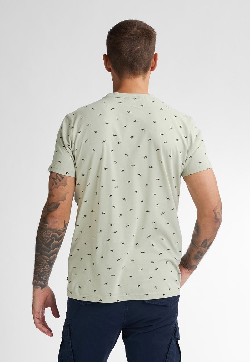 Světle zelené tričko s kulatým výstřihem, krátkými rukávy a opakujícím se černým a tmavězeleným vzorem. Hladký bavlněný materiál s volným střihem.