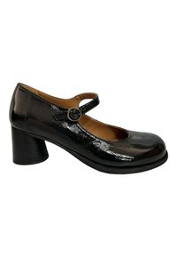 Zapatos Mary Jane de charol negro con punta redonda, tacón de bloque de altura media y una correa delgada asegurada con una hebilla circular.