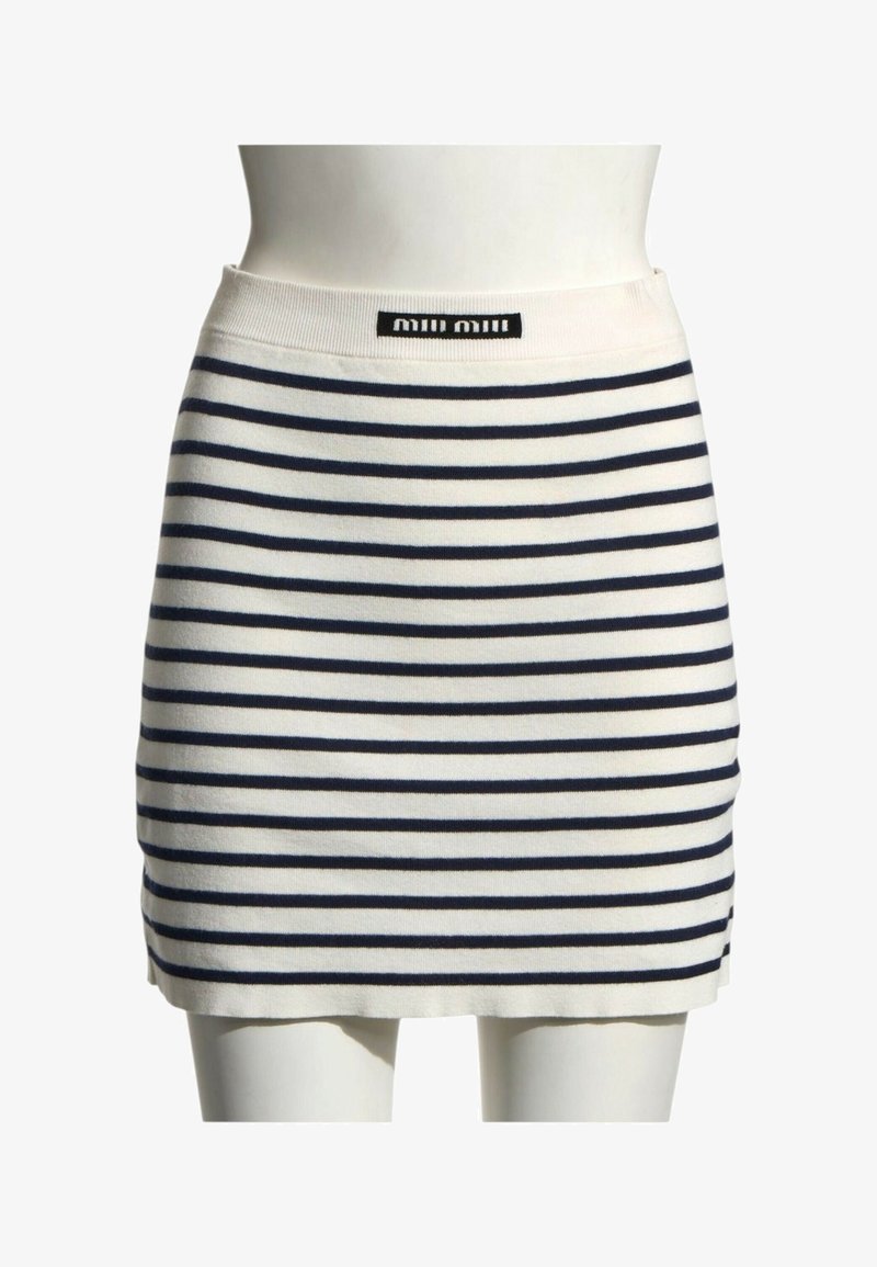 Jupe en maille blanche avec des rayures horizontales bleu marine et une petite étiquette noire à la taille sur un mannequin blanc.