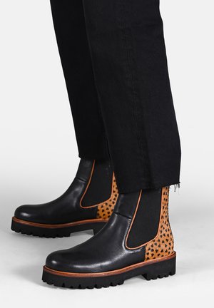 Stivali Chelsea in pelle nera con pannellatura a pois arancioni, inserti elastici laterali e suole in gomma nera robusta. Presentano un bordo marrone a contrasto.