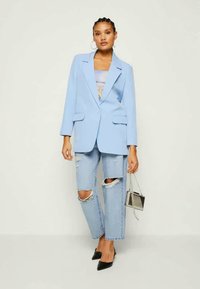 Svetlo modrý blazer so ostrými klopami a dvoma prednými vreckami, spárovaný s poškodenými džínsami, čiernymi lodičkami a malou metalickou kabelkou.