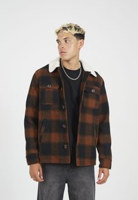 Geruite jas in bruin en zwart, met een contrasterende witte sheepskin kraag, knoopsluiting aan de voorkant en twee borstzakken. Getextureerde stof.