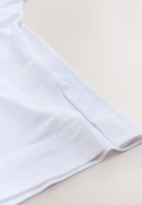 T-shirt blanc en coton, doté d'une texture lisse et d'un ourlet cousu. Le design comprend une coupe décontractée et de petites fentes latérales en bas.
