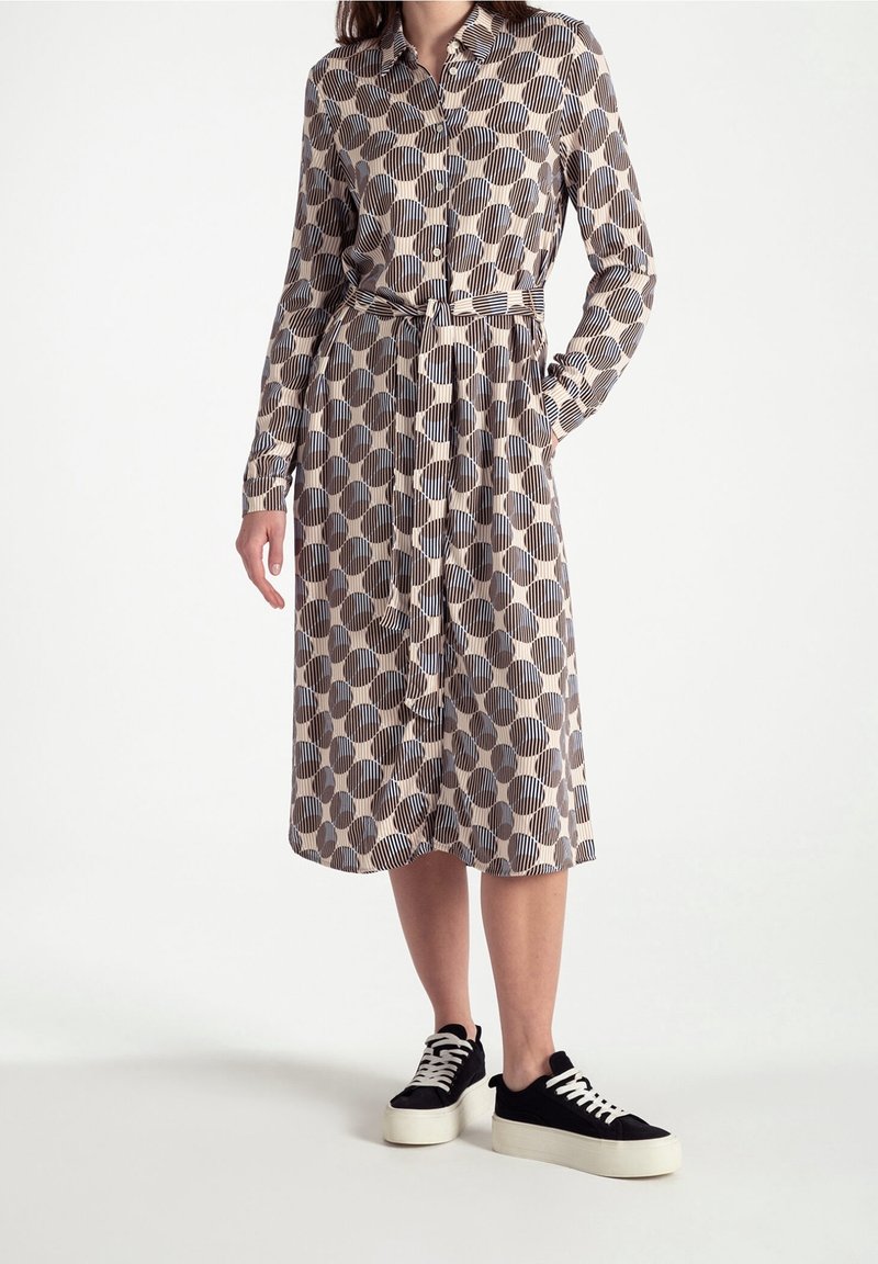 Femme portant une robe midi beige à gros pois marron et noirs et rayures verticales, associée à des baskets compensées noires et blanches.