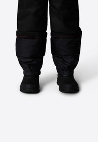 Black insulated snow pants with elastic cuffs and contrasting red stitching, paired with black waterproof boots featuring a textured sole.