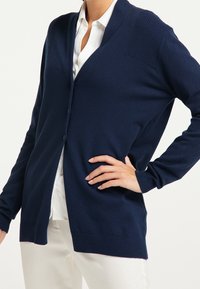 Navyblå kofta i mjukt tyg med v-ringning, knäppning framtill, ribbade axeldetaljer och långa ärmar.