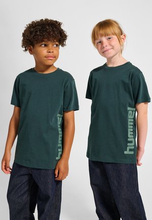 Groene katoenen T-shirts met korte mouwen, met een logoprint in een lichtere groene kleur aan de zijkant, gecombineerd met donkerblauwe spijkerbroeken.