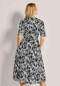 Schwarz-weiß gemustertes Kleid mit kurzen Ärmeln, taillierter Taille und Taschen, aus leicht fließendem Stoff. Rückansicht angezeigt.