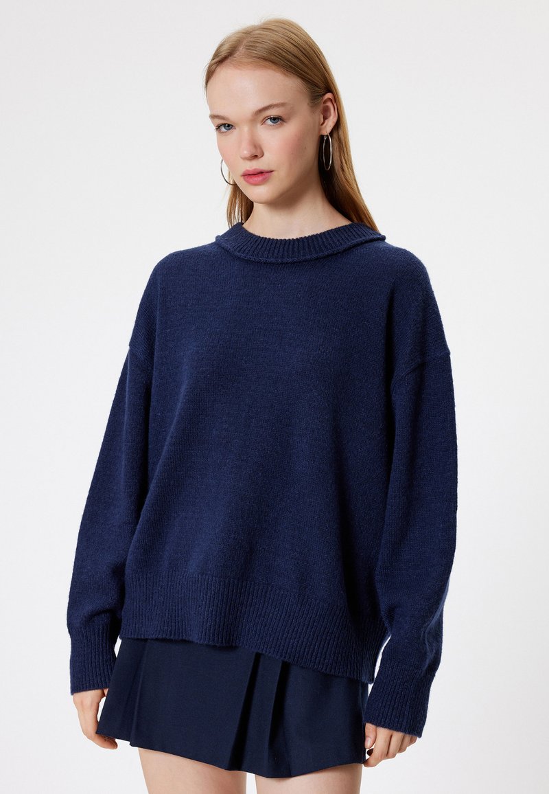 Granatowy, oversize sweter z okrągłym kołnierzem, ściągaczami przy mankietach i u dołu. Miękki w dotyku, luźny krój, zestawiony z granatową spódnicą plisowaną.