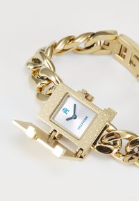 Orologio bracciale con catena d'oro, quadrante squadrato, lancette delle ore e dei minuti blu, e un coperchio a cerniera parzialmente aperto su uno sfondo bianco.