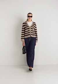 Καρό καρντιγκάν σε καφέ και μπεζ αποχρώσεις, με σχέδιο με κουμπιά μπροστά. Συνδυασμένο με σκούρα τζιν παντελόνια και μαύρα γυαλιά ηλίου, κρατώντας μια τσάντα με πουά μοτίβο.