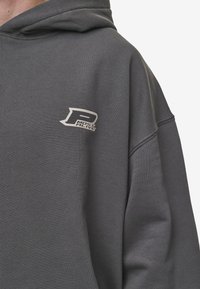 Felpa grigia con cappuccio, caratterizzata da un piccolo logo grigio chiaro. Realizzata in un materiale morbido con una vestibilità ampia e rilassata.