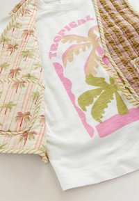 T-shirt blanc avec un graphique tropical de palmiers roses et verts. Enveloppé dans un gilet à motifs avec des rayures roses et des motifs de palmiers, tissu texturé.