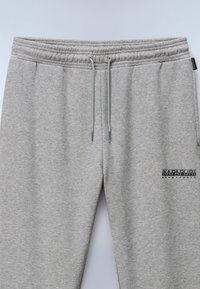 Hellgraue Sweatpants aus weichem Material mit einem elastischen Bund und Kordelzug sowie einem Logo auf dem linken Oberschenkel.