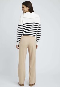 Pull en tricot rayé blanc et marine avec un col replié, associé à un pantalon large beige. Tissu lisse et coupe ajustée.