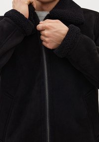 Sort jakke med en tekstureret, faux-shearling krave og manchetter. Har en frontlynlås og sidelommer. Blødt, suede-lignende materiale.