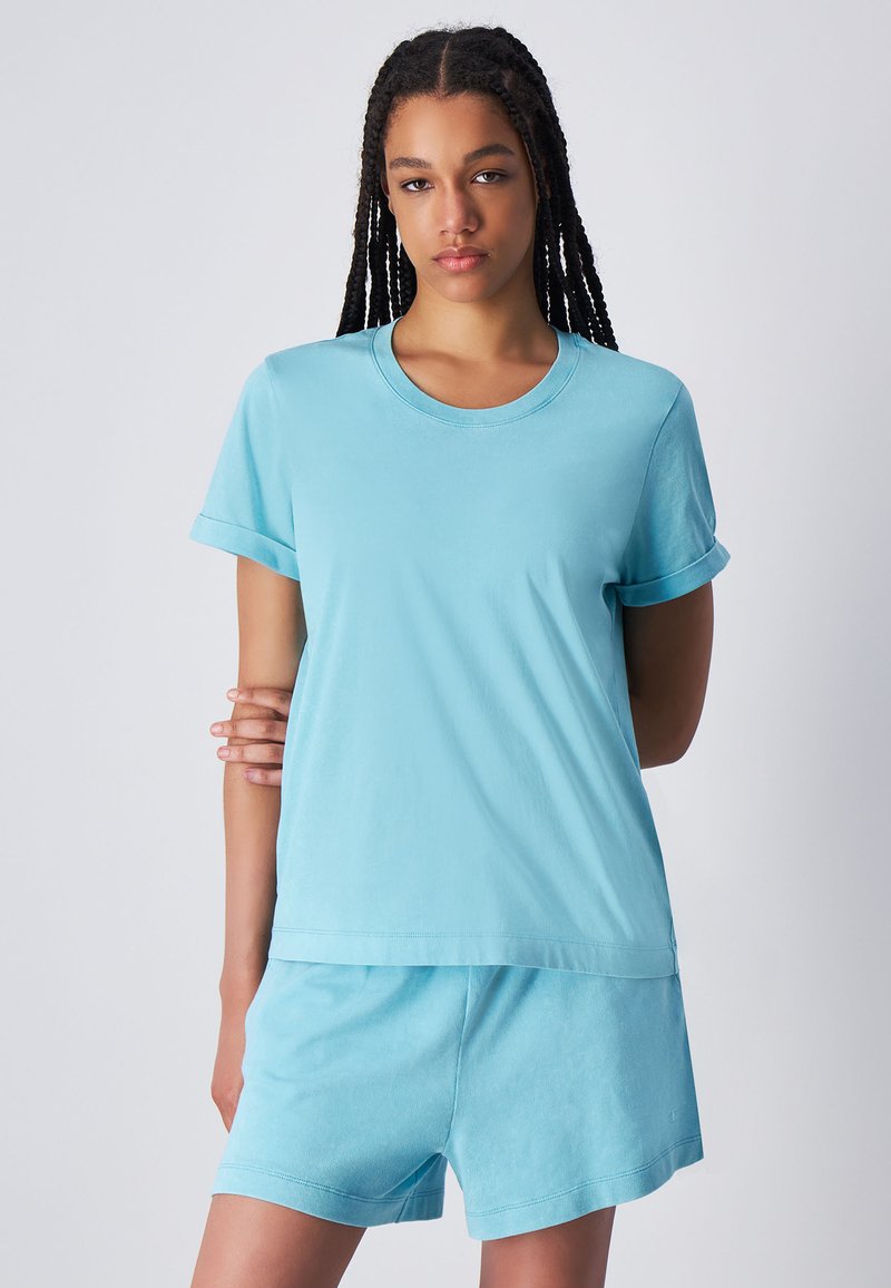 Maglietta in cotone azzurra chiara con maniche corte arrotolate, scollatura rotonda e vestibilità comoda, abbinata a pantaloni corti blu coordinati.