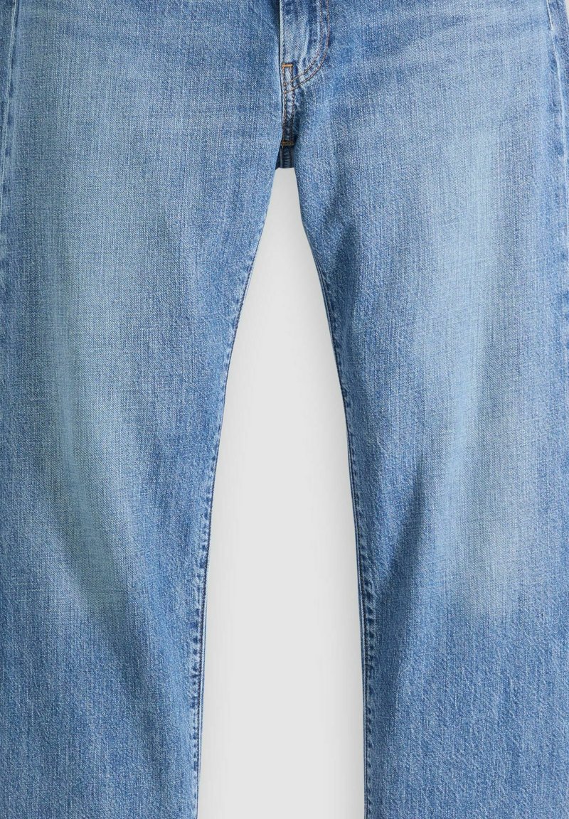 Jean en denim bleu clair avec fermeture éclair avant visible et coutures apparentes, présenté à plat sur un fond blanc.