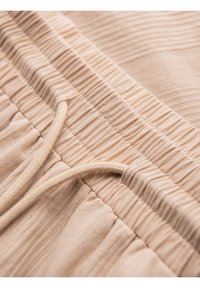 Ceinture élastique beige avec tissu froncé et cordon sur un vêtement doux et léger.