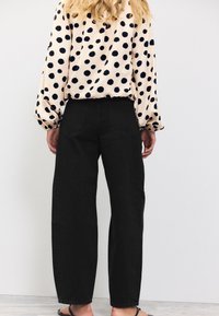 Prickig blus med puffärmar i creme och marinblått. Högmidjade svarta jeans med avslappnad passform och synliga bakfickor.