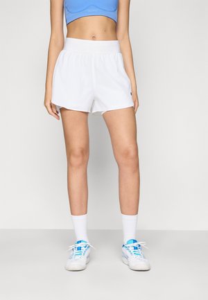 Pantalones cortos deportivos blancos con una cinturilla elástica, textura suave y un pequeño detalle de logo, combinados con zapatillas azules y calcetines blancos.