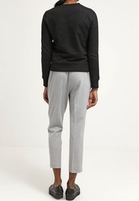 Czarny sweatshirt z długimi rękawami, okrągłym dekoltem, w połączeniu z jasnoszarymi zwężającymi się spodniami i czarnymi butami na platformie, widok z tyłu.