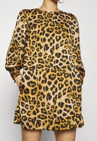 Leopard print dress with three-quarter sleeves, a round neckline, and pockets. Features a smooth, shiny fabric in gold and black tones.