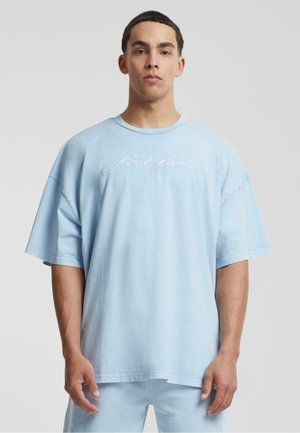 Light blue oversized t-shirt made from soft cotton with a crew neckline, featuring white cursive "Karl Kani" text on the front.
