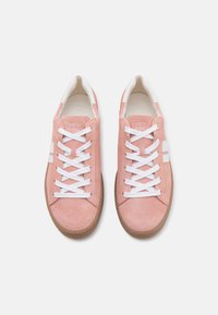 Vaaleanpunaiset mokkasneakerit, joissa on valkoiset nauhat ja sivunauhat. Ne koostuvat tekstuuripinnasta ja ruskeasta kumipohjasta. Pehmeä, rento muotoilu.