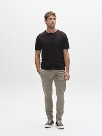 Mustad lühikeste varrukatega T-särk koos beežide kitsaste pükstega ning must-valgete triibuliste tossudega. Lihtne taust, neutraalne valgustus.