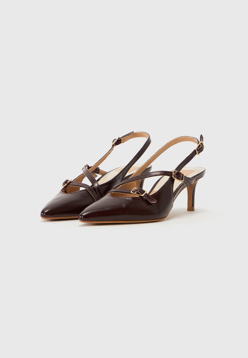 Tacones slingback de cuero marrón con punta afilada, finas correas en el tobillo y accesorios de hardware dorado. Tacones pequeños y afinados. Textura suave.