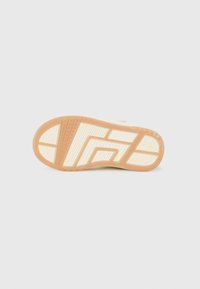 Semelle en caoutchouc avec un design multi-texturé. Accents colorés en beige et crème, présentant des motifs distincts pour l'adhérence et la traction.
