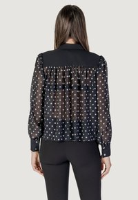 Blusa trasparente nera a pois con maniche a sbuffo e retro arricciato, caratterizzata da una parte superiore nera uniforme e polsini con bottoni.