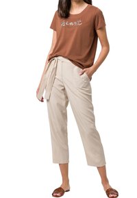 Brun kortærmet t-shirt med et dekorativt frontprint, parret med lysebeige, højtsiddende, vide bukser og brune sandaler.