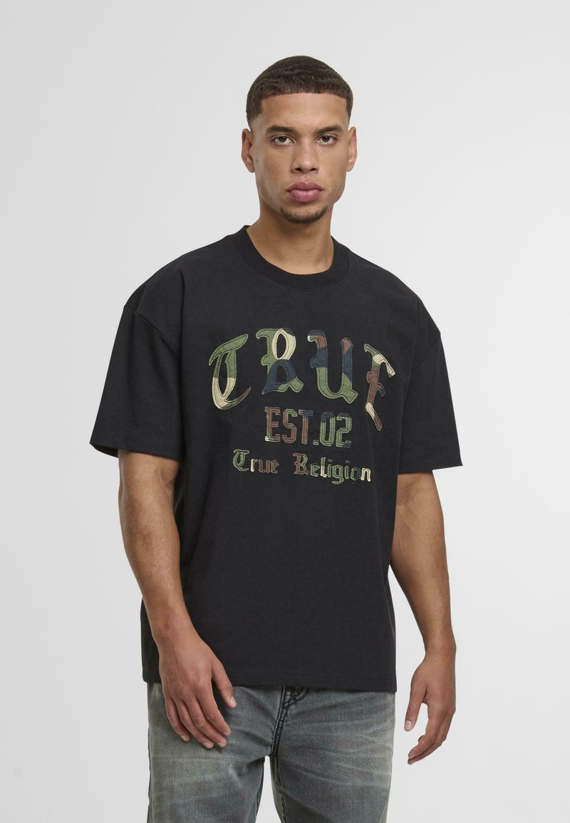 Camiseta de algodón negra de manga corta y cuello redondo. Presenta un texto de camuflaje colorido: "TRUE EST.02 True Religion" en la parte delantera.