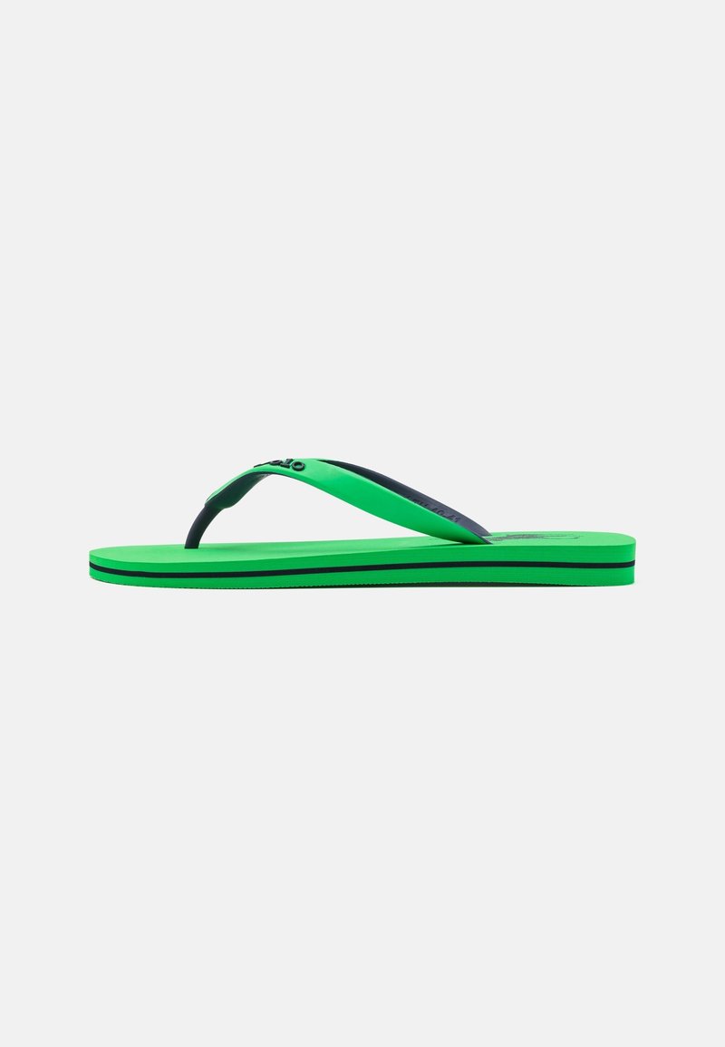 Tongs vertes avec une bande noire sur la semelle et une lanière noire et verte, vues de côté sur fond blanc.